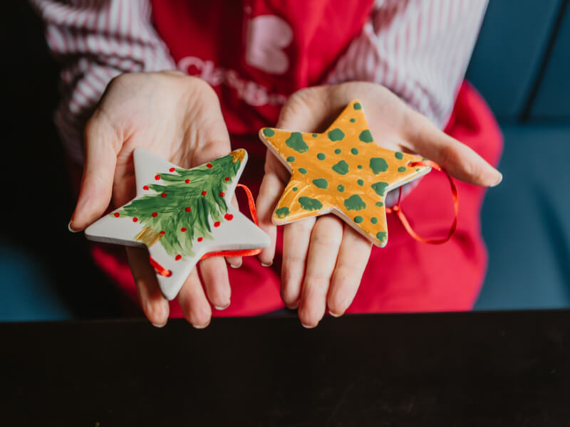 A close up of two hands holding two hand painted Christmas stars